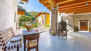 Un espacio al aire libre techado con una mesa, sillas, un banco y vistas a una colina con edificios.