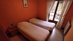 Una habitación con dos camas, una mesita de noche, una lámpara y una ventana con cortinas.