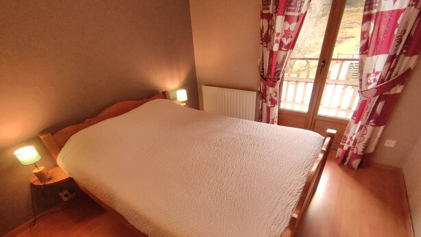 A bedroom with a bed, bedside lamps, a window with curtains, and a radiator.