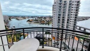 A balcony with a view of a river, a tall building, and a small table. - Chevron Renaissance, 2BR w/ Views, Parking & WIFI (Gold Coast)