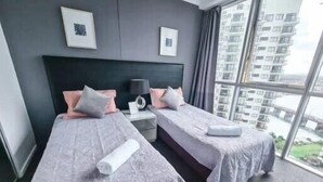 A hotel room with two beds, grey bedding, a large window with a view of high-rise buildings, and framed pictures on the wall. - Chevron Renaissance, 2BR w/ Views, Parking & WIFI (Gold Coast)