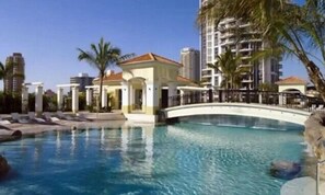 A swimming pool with a bridge, palm trees, and modern buildings in the background. - Chevron Renaissance, 2BR w/ Views, Parking & WIFI (Gold Coast)