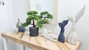 A wooden console table with a potted bonsai tree, a whale tail sculpture, and a white decorative piece. - Chevron Renaissance, 2BR w/ Views, Parking & WIFI (Gold Coast)