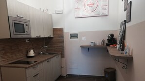 Una cocina compacta con microondas incorporado, un lavamanos y una pequeña encimera. Hay una cafetera y una botella de detergente para platos sobre la encimera.