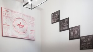 Una cocina con cafetera, lavamanos y cubo de basura. Hay adornos en la pared, incluyendo un calendario y letreros con frases como 'EAT, DRINK, LIVE'.