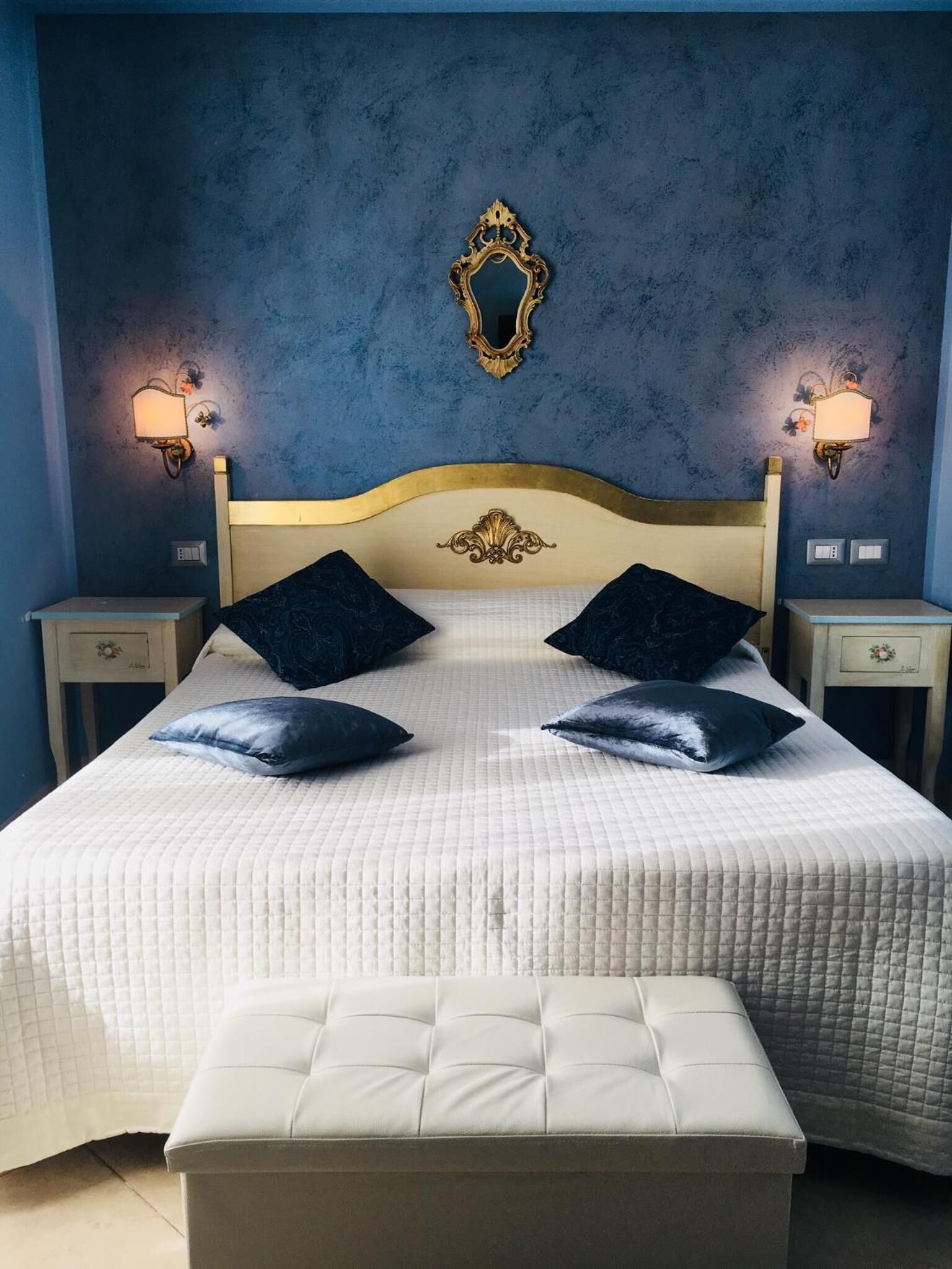 A bed with a white quilted bedspread, two dark pillows, and a tufted headboard.