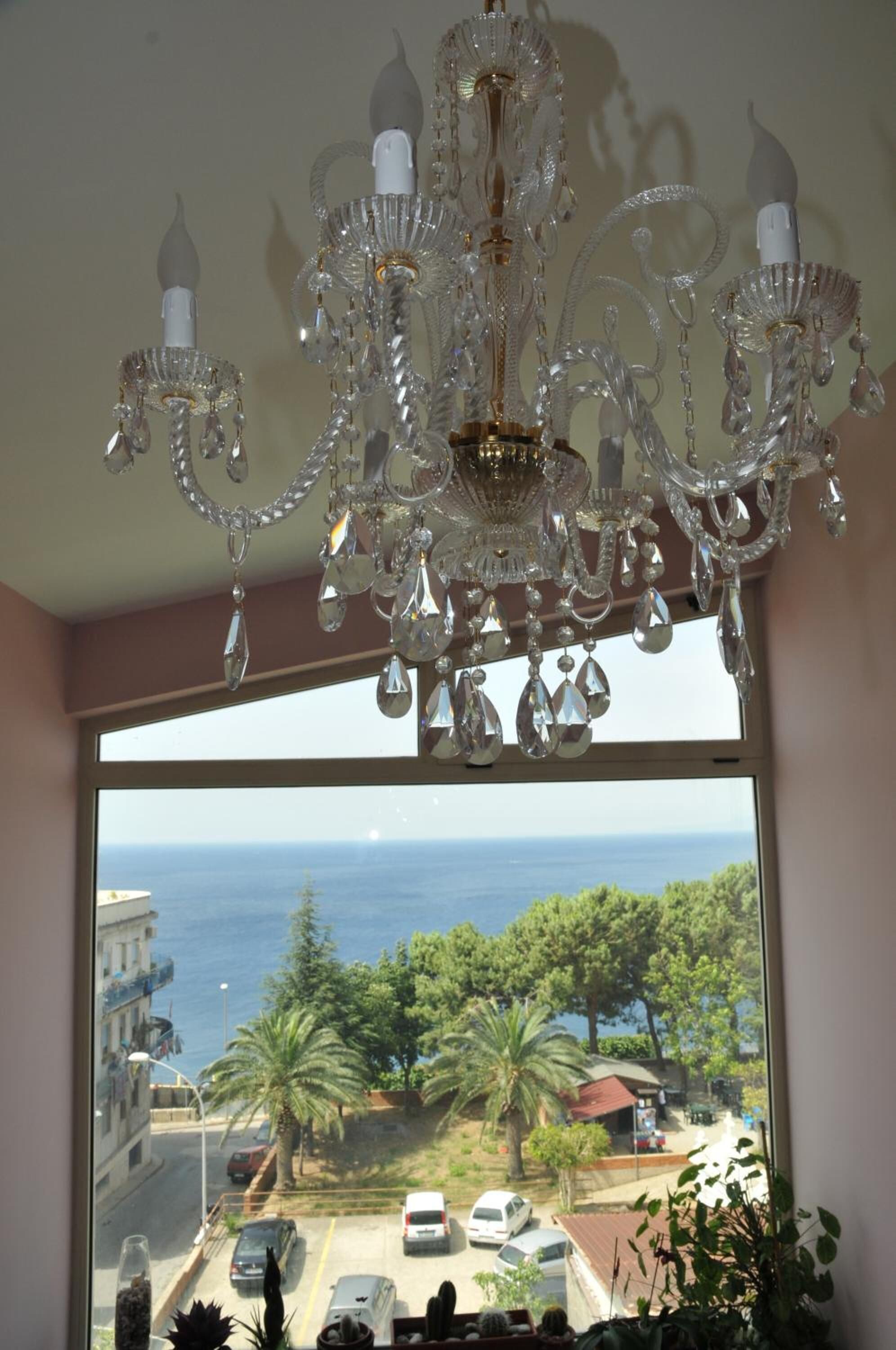 A room with a large window overlooking a coastal area, featuring a chandelier.