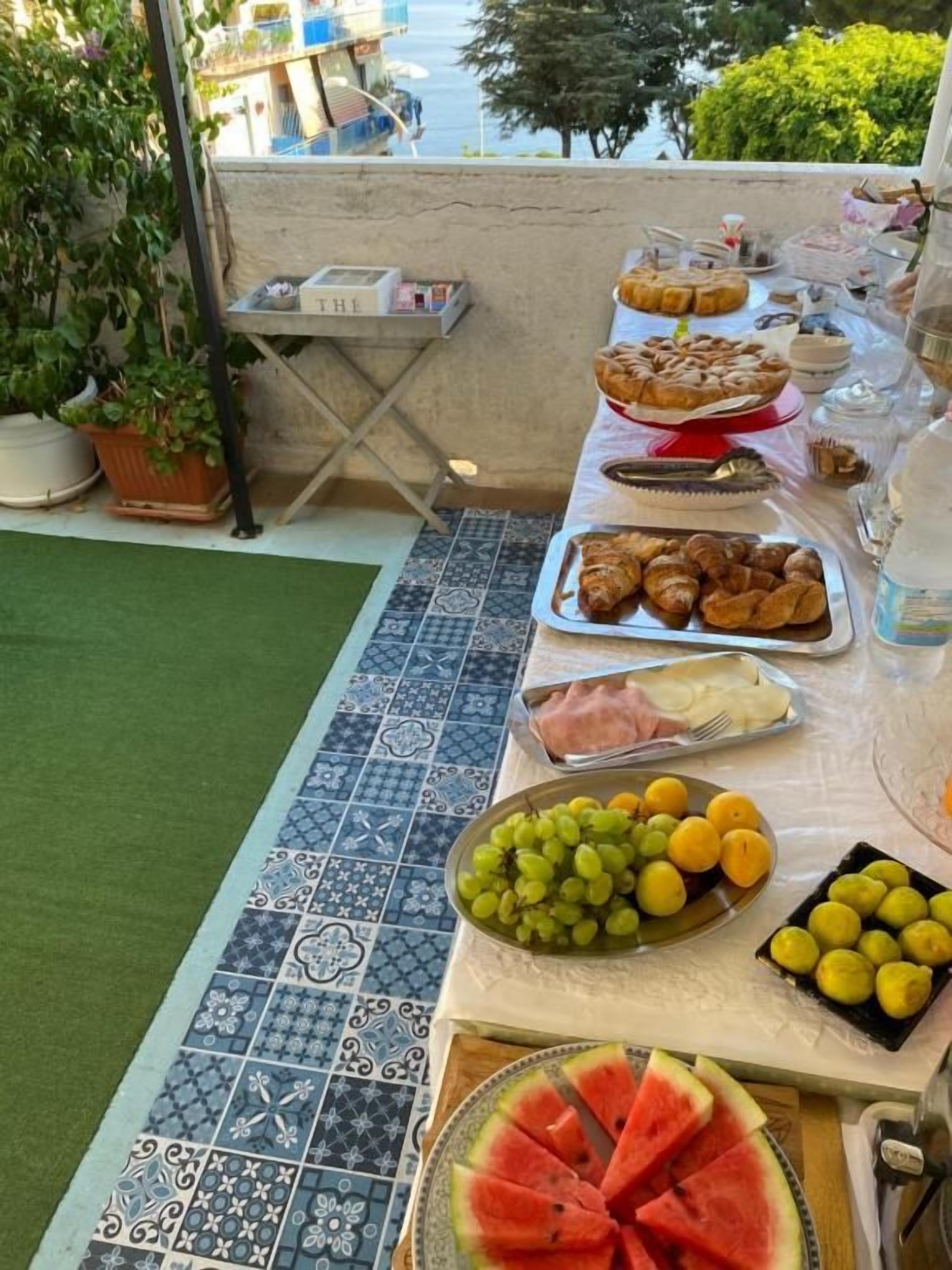 Et bord med forskellige spiser, herunder frugter, kager og en vandmelon.