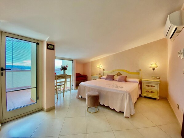 Un dormitorio con cama, mesitas de noche, una silla y vistas a través de una puerta.