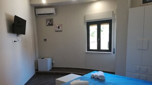 Una habitación de hotel con cama, ventana, aire acondicionado y una mesita.