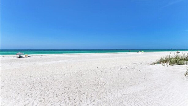 Une vaste plage de sable fin, avec une eau d’un bleu limpide et un ciel dégagé.