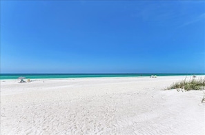 A wide sandy beach with clear blue water and a clear sky.