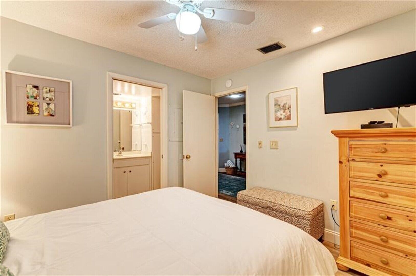 A bedroom with a bed, a wooden dresser, a television, and a ceiling fan.