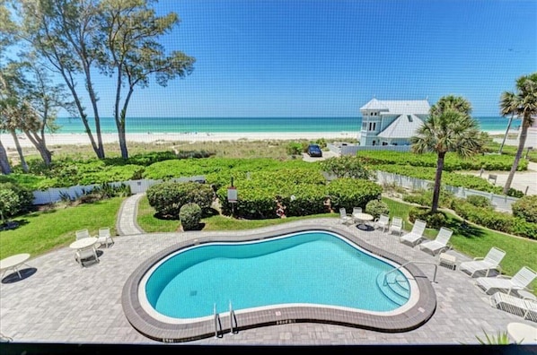 A swimming pool with lounge chairs and a view of the beach and ocean.