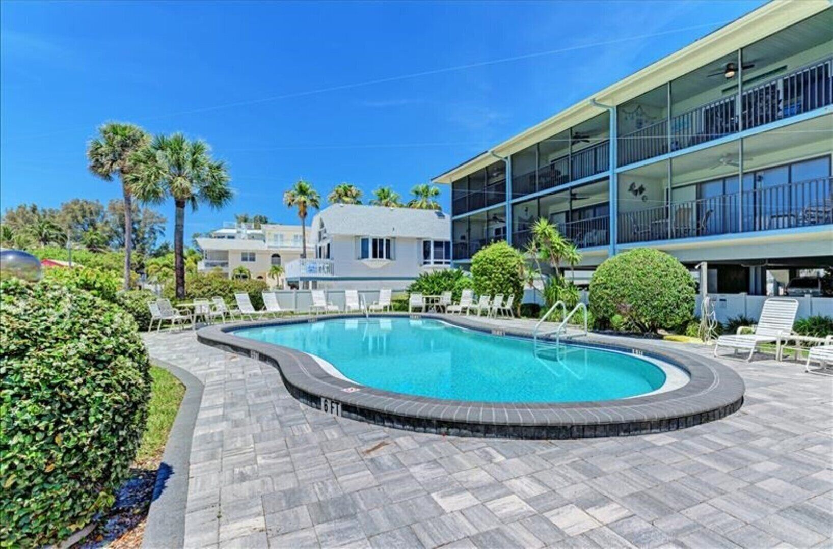 A swimming pool with a curved edge, surrounded by lounge chairs and a building with balconies.