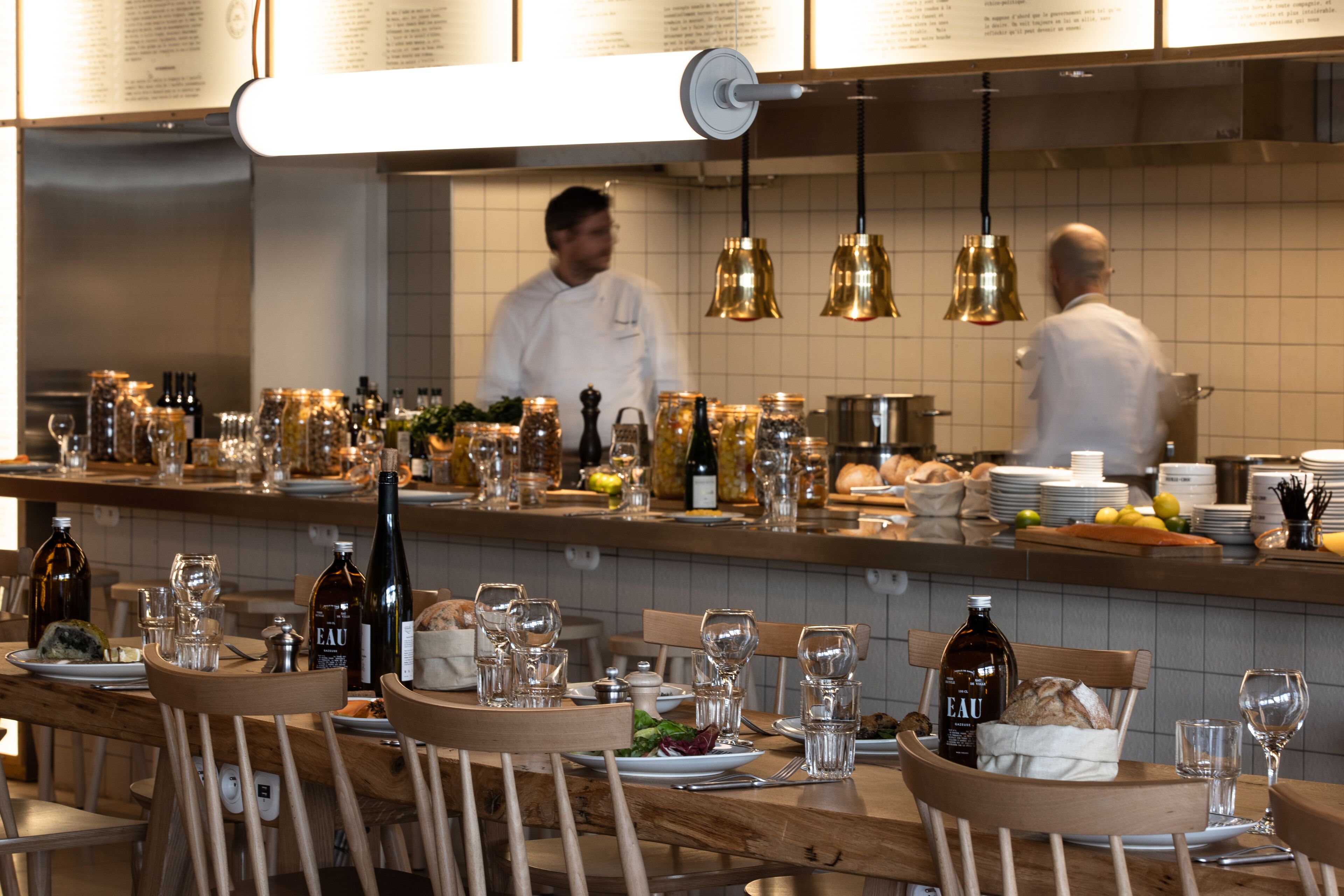 A restaurant interior with wooden tables, chairs, and a counter with various bottles and glasses.