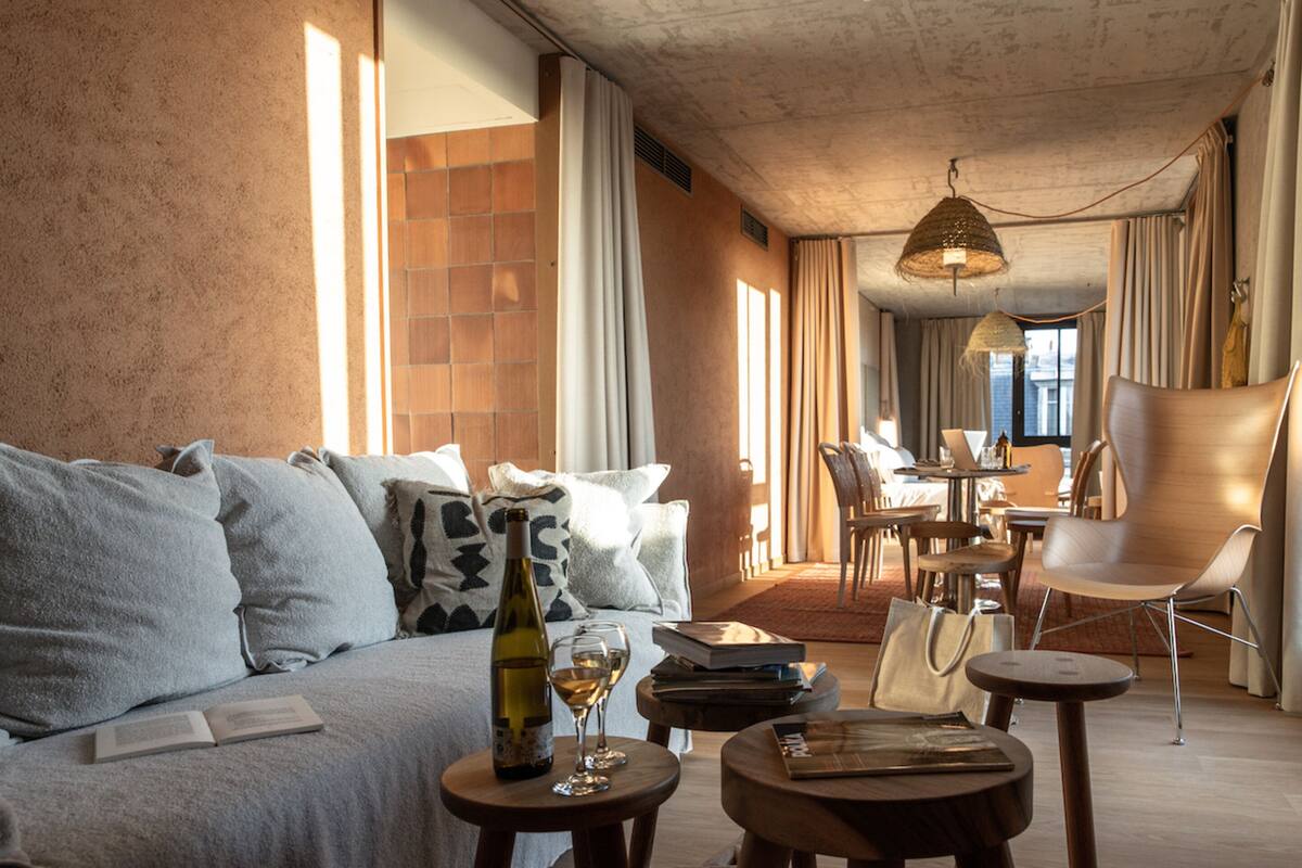Una sala moderna con un sofá, una mesita con una botella de vino y una copa, y un comedor con sillas y una mesa.