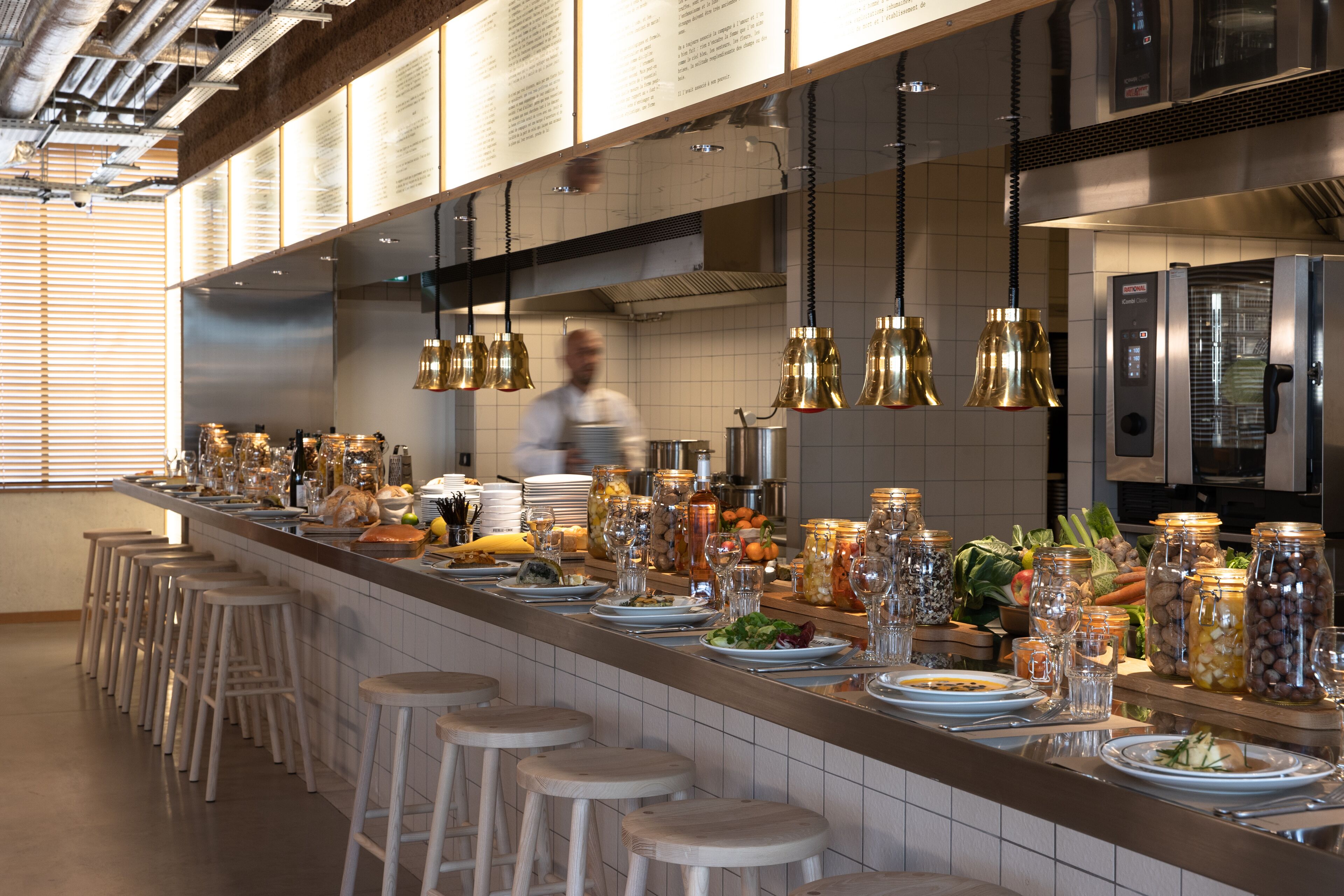 Une cuisine moderne avec un long comptoir, des tabourets et des luminaires suspendus.