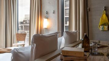 A hotel room with a bed, a bedside table with books, a bottle, and a glass.