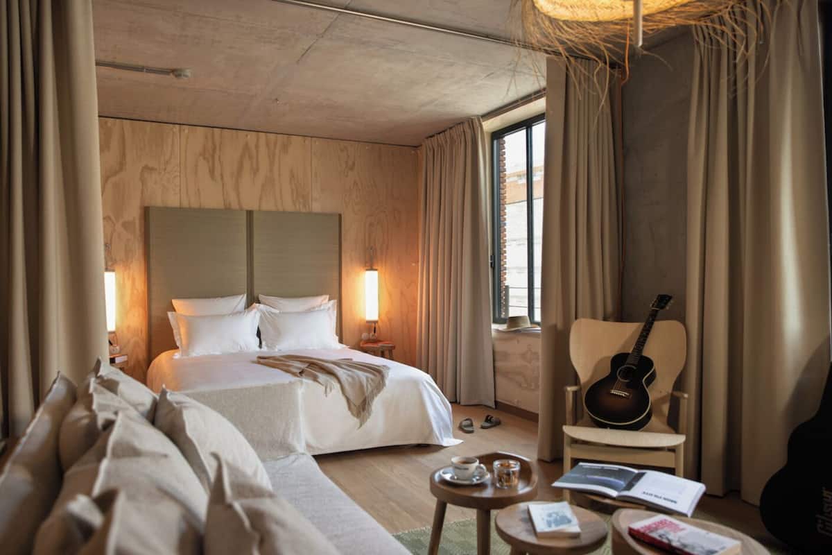 Habitación de hotel con cama, sofá, una guitarra y una mesita con libros y una taza.
