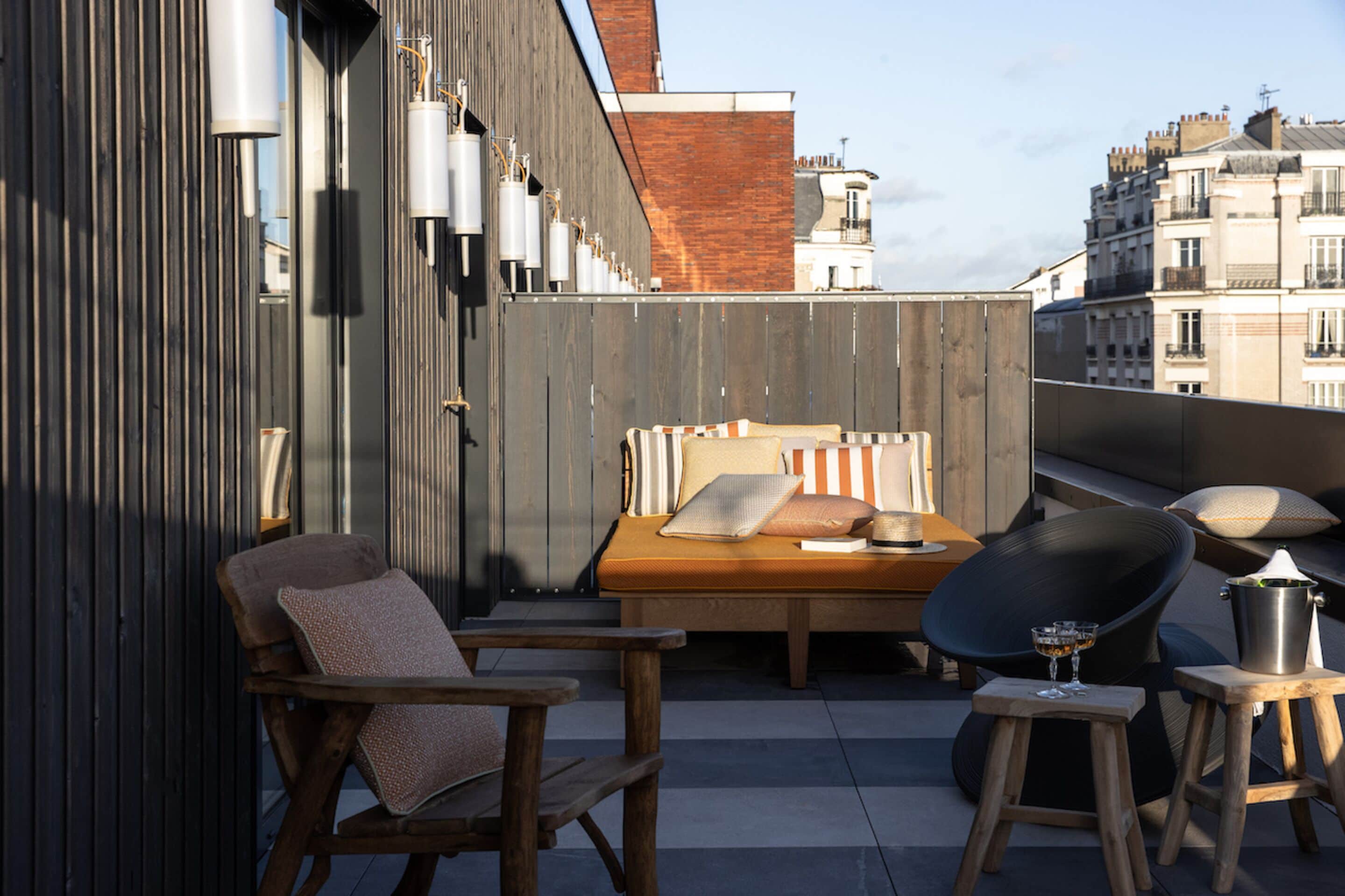 A rooftop terrace with a bed, two chairs, and a small table with drinks.