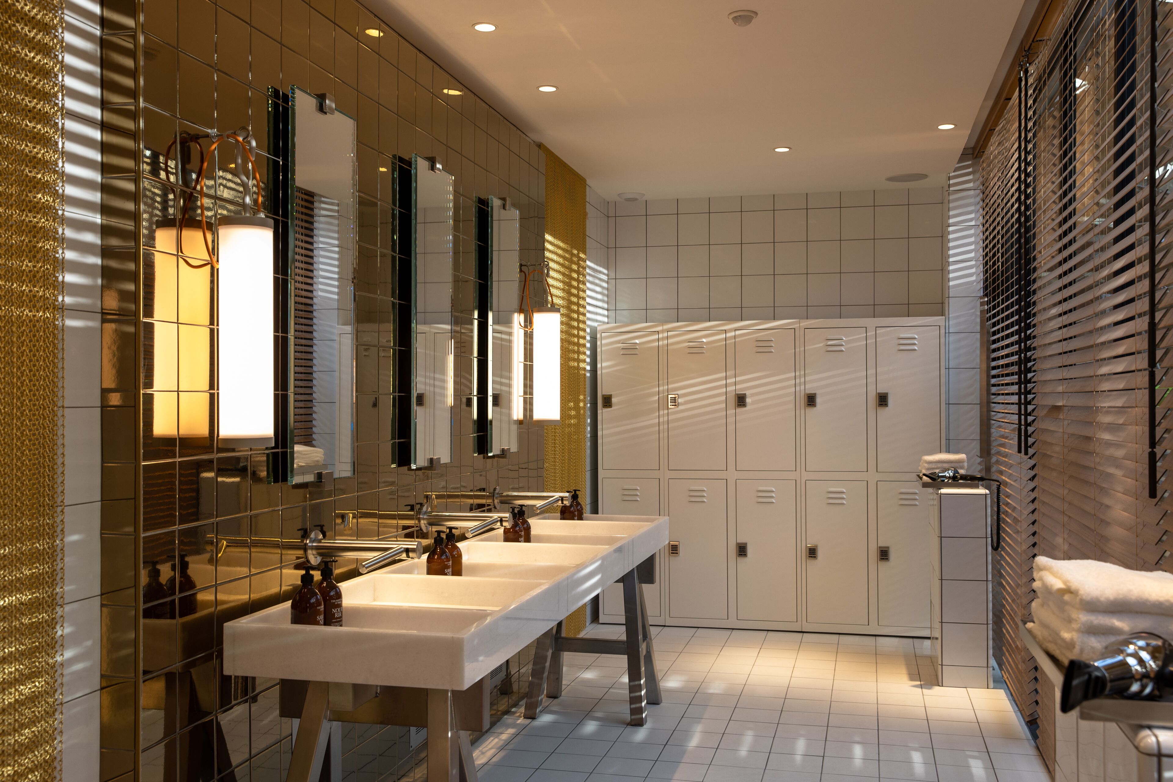 A modern bathroom with two sinks, mirrors, and a row of lockers.