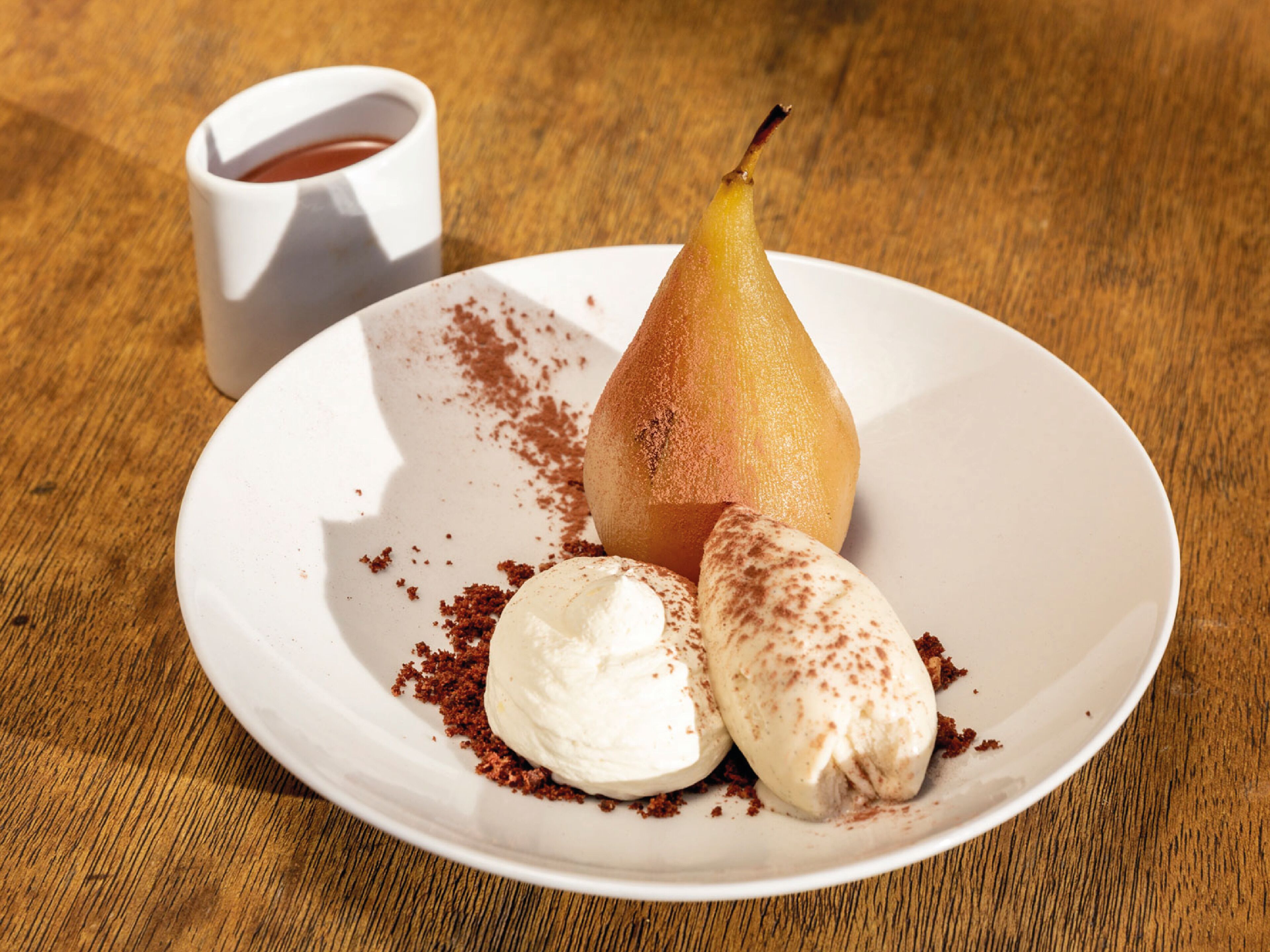 A dessert plate with a pear, ice cream, and crumbs on a wooden table.