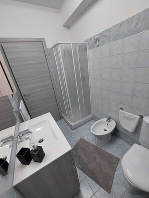 A modern bathroom with a shower, sink, bidet, and toilet. - Focu e Mari (Mascali)