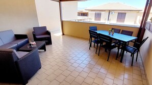 A balcony with a dining table and chairs, a sofa, and a small table with a bottle and glasses. - Focu e Mari (Mascali)