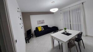 A dining area with a white table, four chairs, and a black sofa with a yellow pillow. - Focu e Mari (Mascali)