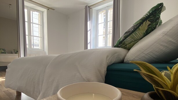 A bedroom with a bed, a bedside table with a candle, and a window with curtains. - Maison Saint Louis (Poitiers)