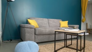 A living room with a grey sofa, two yellow cushions, a blue knitted pouf, a wooden coffee table, and a floor lamp. - Maison Saint Louis (Poitiers)