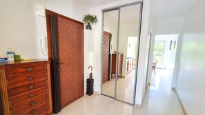 Un pasillo con un aparador de madera, una puerta corredera y un espejo que refleja una habitación con una mesa y sillas.