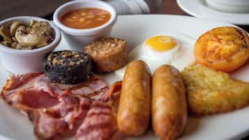 A plate of breakfast food including sausages, eggs, bacon, mushrooms, beans, and a grilled tomato.