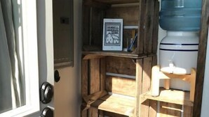 A narrow hallway with wooden crates stacked as shelves, a water dispenser, and a framed sign on the wall. - Grinnell Heritage Tiny House - On Organic Farm (Grinnell)