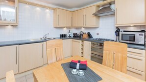 Una cucina moderna con mobili chiari in legno, un piano di lavoro nero, elettrodomestici in acciaio inossidabile e un tavolo da pranzo con sottotavola.