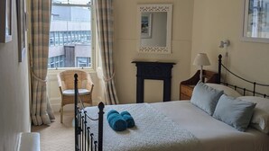 Ein Schlafzimmer mit Bett, Stuhl, Nachttisch, Lampe und einem Fenster mit Vorhängen.