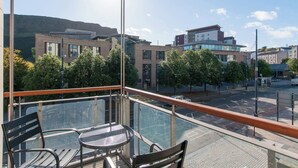 En balkong med ett glasräcke som vetter ut mot en stadsgata, med moderna byggnader och träd i utsikten.
