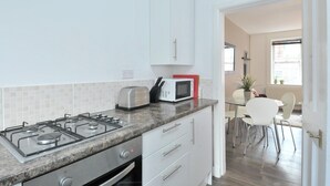 Una cocina moderna con estufa a gas, microondas y tostadora. Hay armarios blancos y un comedor con mesa y sillas.