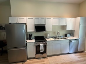 A compact kitchen with white cabinets, a stainless steel refrigerator, a microwave, a stove, a dishwasher, and a toaster.