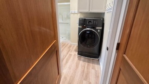 Une buanderie équipée d’un lave-linge et d’un sèche-linge à chargement frontal, de meubles en bois et d’un sol carrelé.
