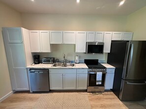 Cocina compacta con armarios blancos, refrigerador de acero inoxidable, microondas, tostadora, pileta y lavavajillas.