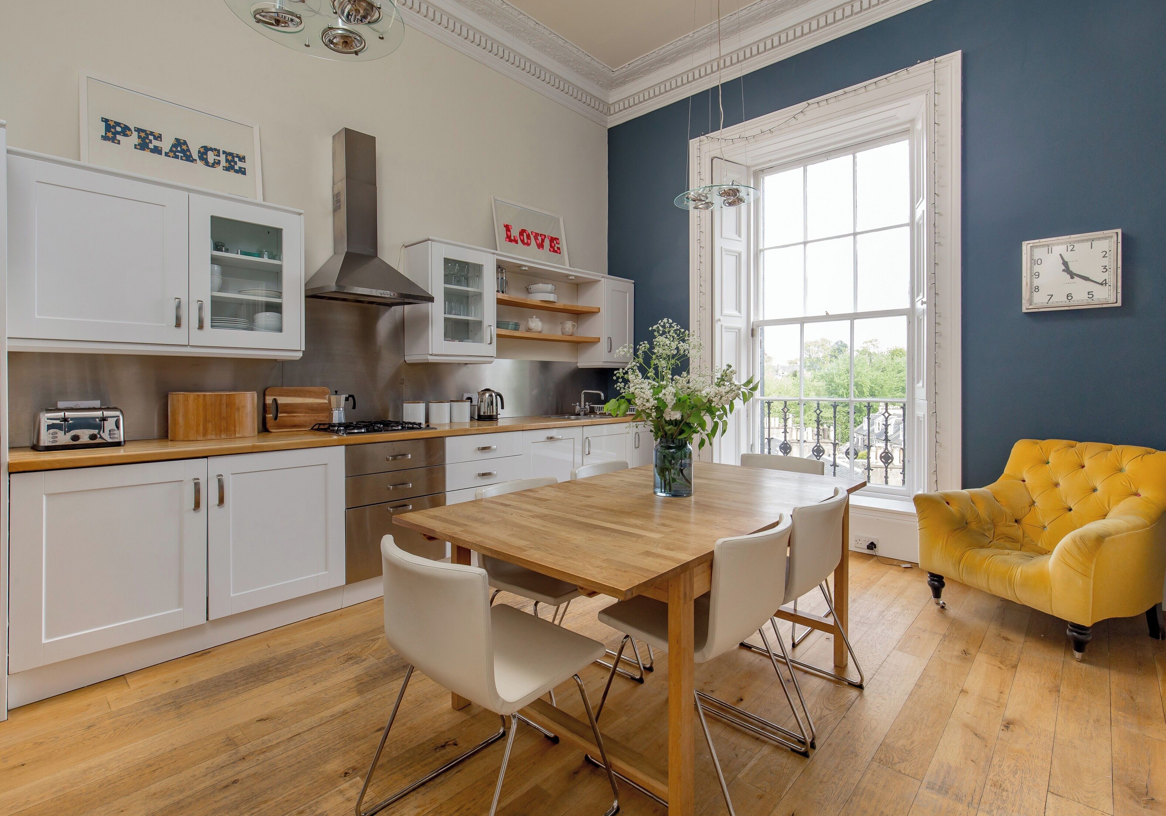 A modern kitchen with white cabinetry, a wooden dining table, and a yellow armchair.