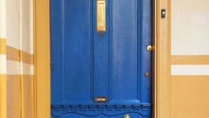 Una puerta azul con un tirador y buzón de latón, enmarcada por paredes amarillas y un felpudo marrón.