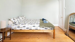 Una cama individual con una colcha estampada, una lámpara de noche y un espejo a la derecha.