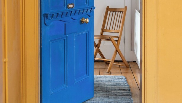 Una puerta azul con un picaporte de latón y una placa pequeña de latón, una silla de madera y una alfombra azul sobre un piso de madera.