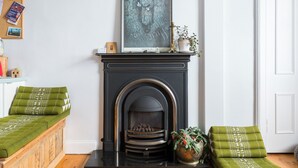 Una habitación con chimenea, un sofá verde, un pouf verde y una obra de arte enmarcada sobre la chimenea.