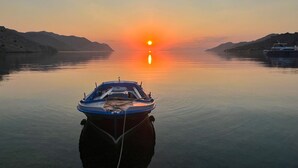 Un barco fondeado en aguas tranquilas durante el atardecer, con cielo despejado y montañas distantes.