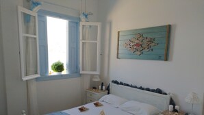 Un dormitorio con una cama, dos mesitas de noche, un velador, una ventana con contraventanas abiertas y una obra de arte colgada en la pared.