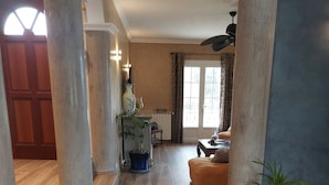 A spacious hallway with wooden flooring, a potted plant, a table with a bowl of fruit, and a large window with curtains. - -Bright villa, pool, air conditioning, near St-Florent- sleeps 6 (Oletta)
